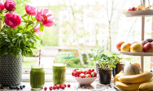 Grüne Smoothies Set-up auf der Fensterbank mit vielen Früchten und Blick ins Grüne.