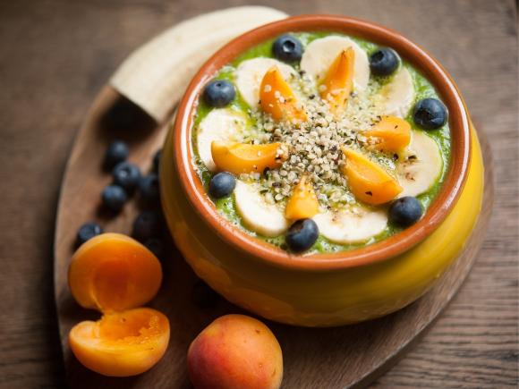 Grüner Smoothie in einer Schale mit Topping aus Pfirsich, Blaubeeren, Bananen und Hanfsamen