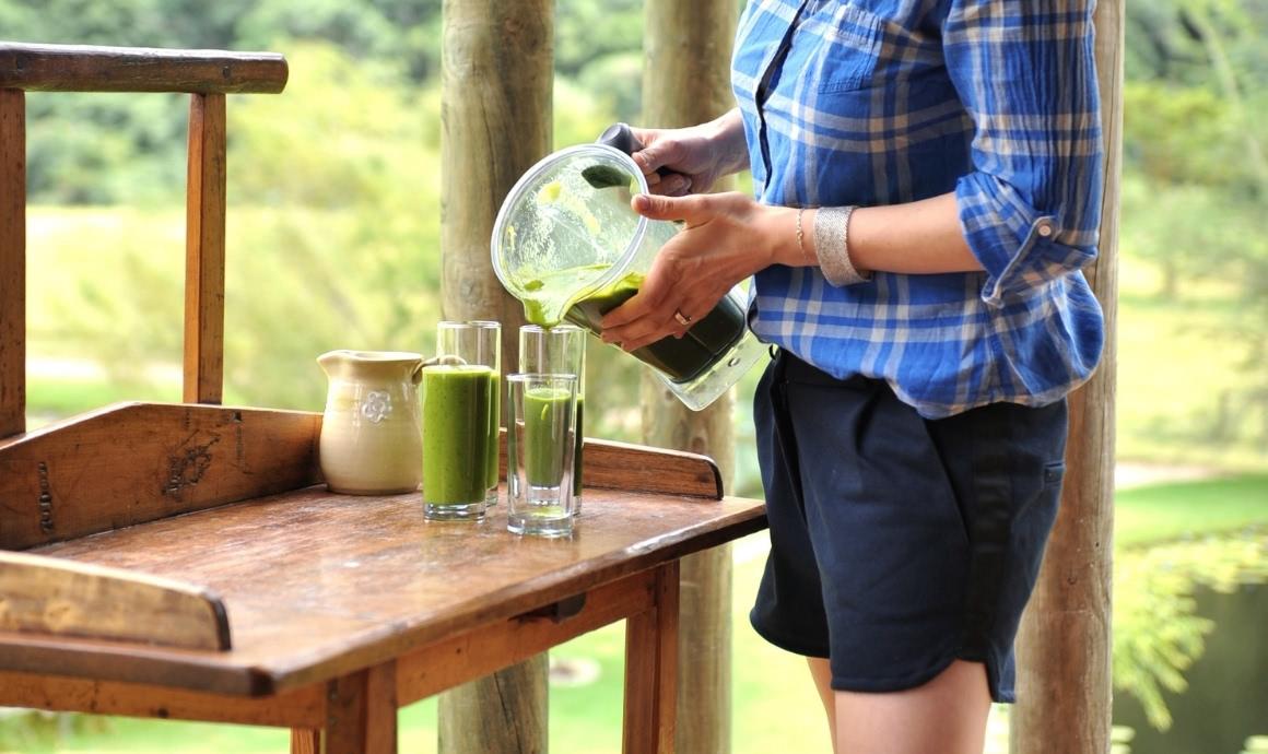 Frau gießt Grüne Smoothies aus dem Mixbehälter in Gläser.