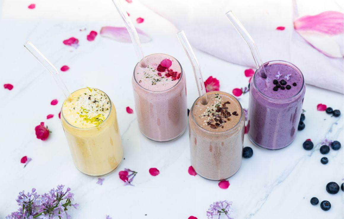 Vier verschiedenene Protein Shakes seitlich von oben fotografiert auf weißer Tischplatte