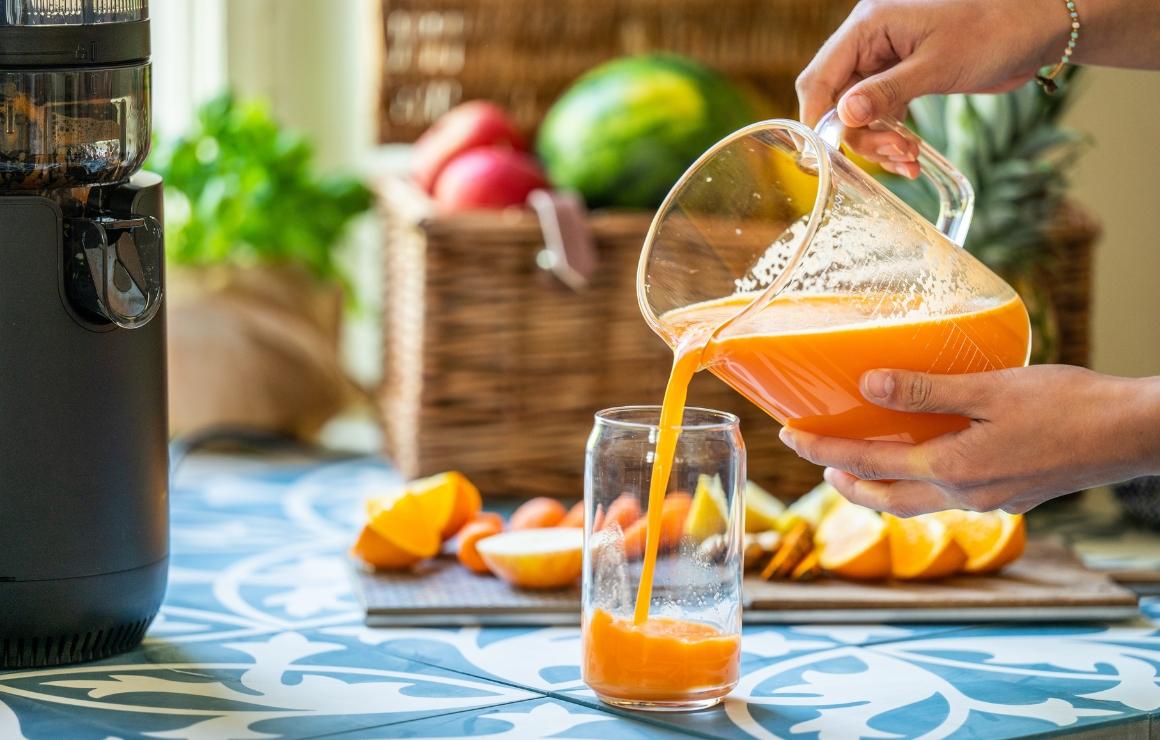 Viasus Flow M steht links, rechts davon wird der frisch gepresste, klare Karottensaft in ein Glas gegossen